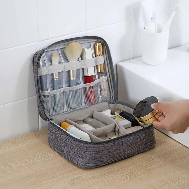 A gray cosmetic organizer displaying makeup brushes, lipsticks, and skincare products, with a hand reaching for a gold compact.
