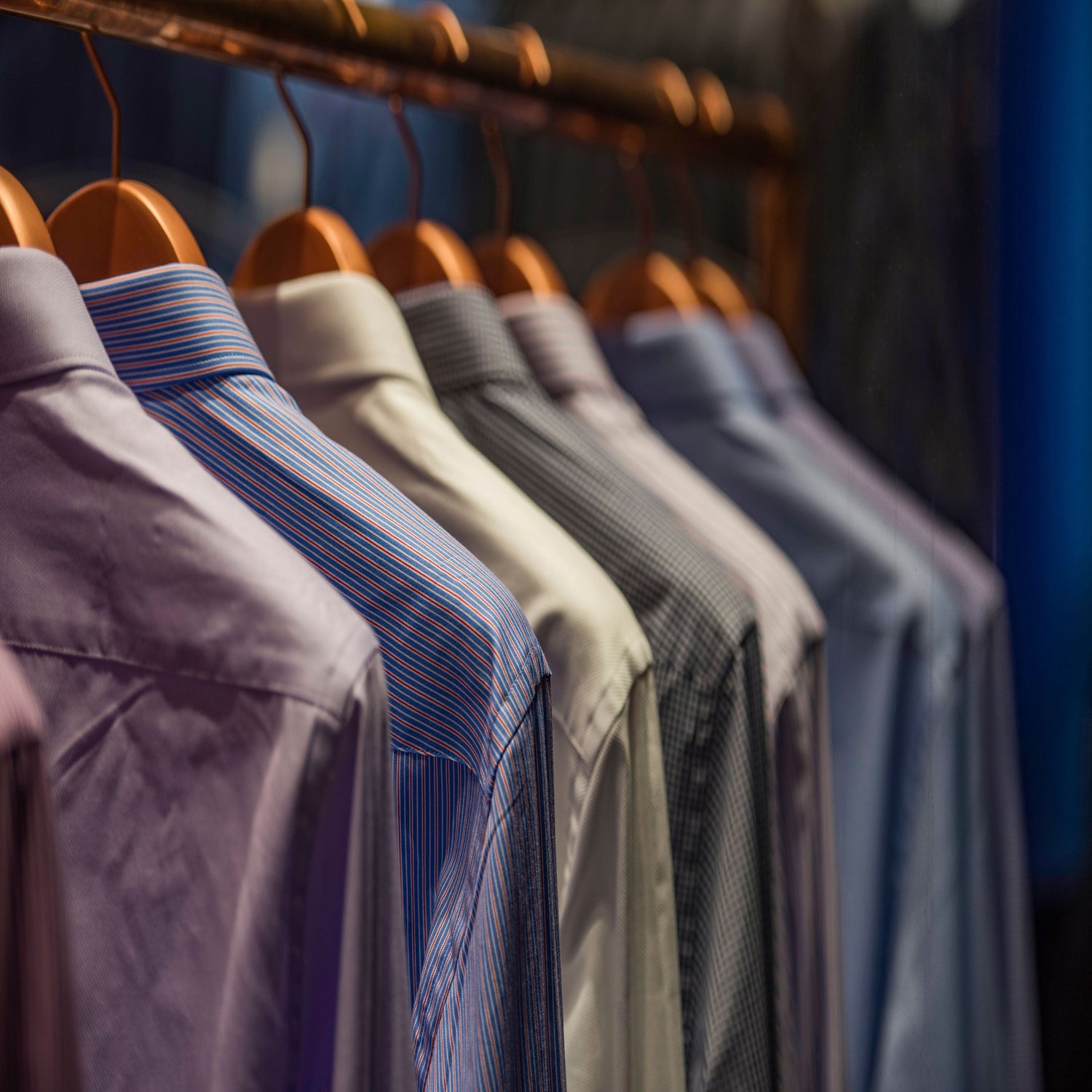 Seven men's shirts hanging on a clothes rack.