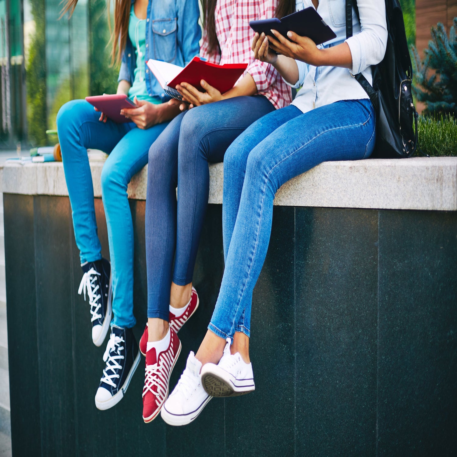 Three women sitting on a wall modelling jeans.