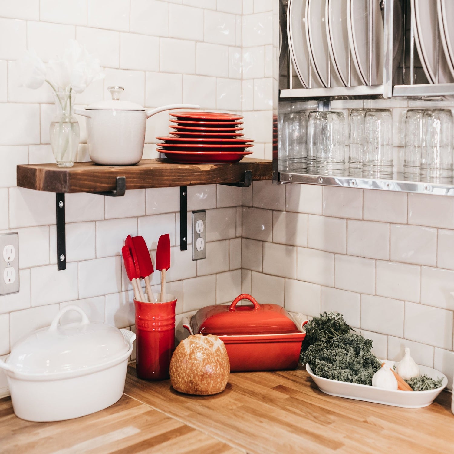 Bright white kitchen with wood bench displaying kitchen pots, pans, plates and utensils.