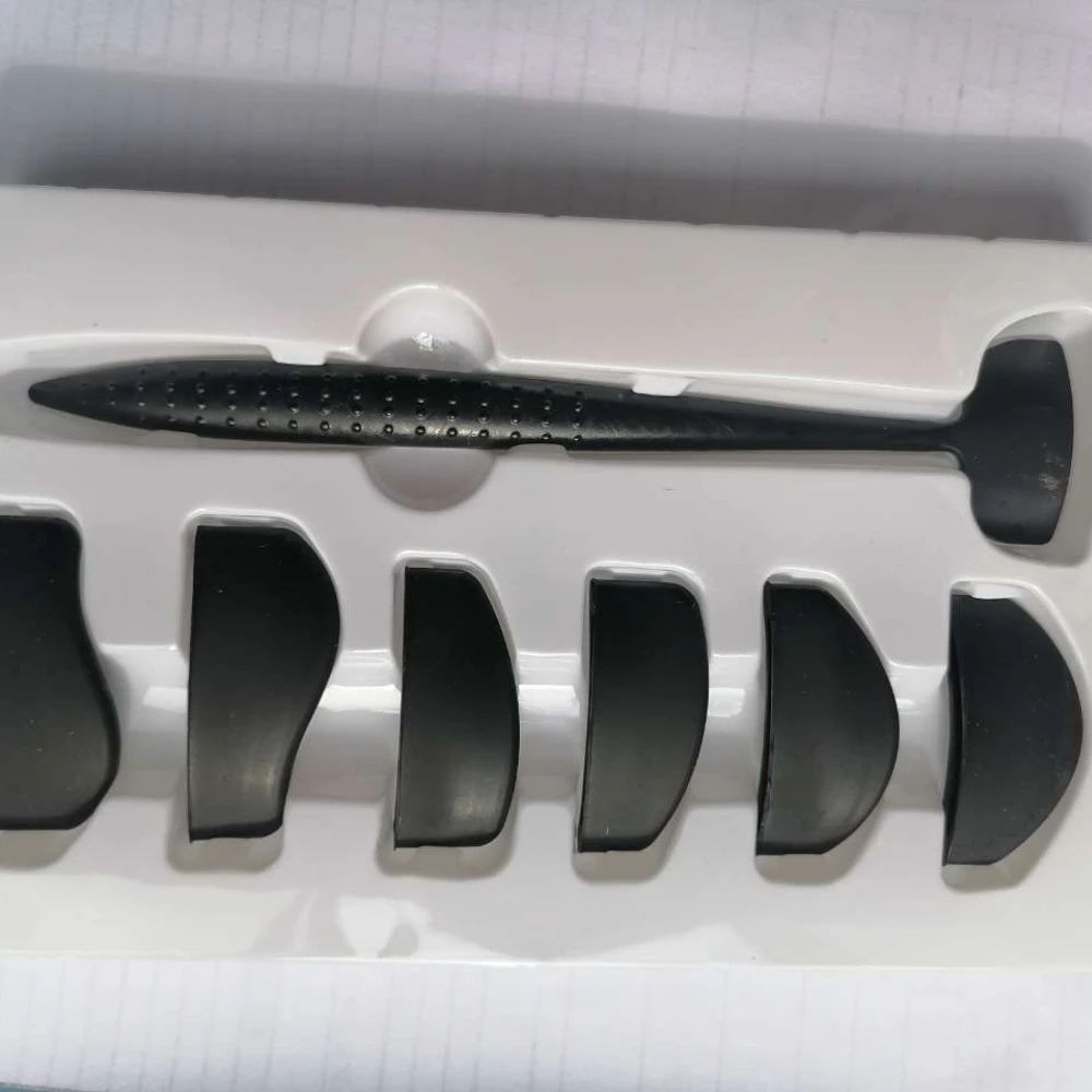 A black fin model kit against a white plastic holder, showing one large and several smaller fins. The setup suggests assembly or display.