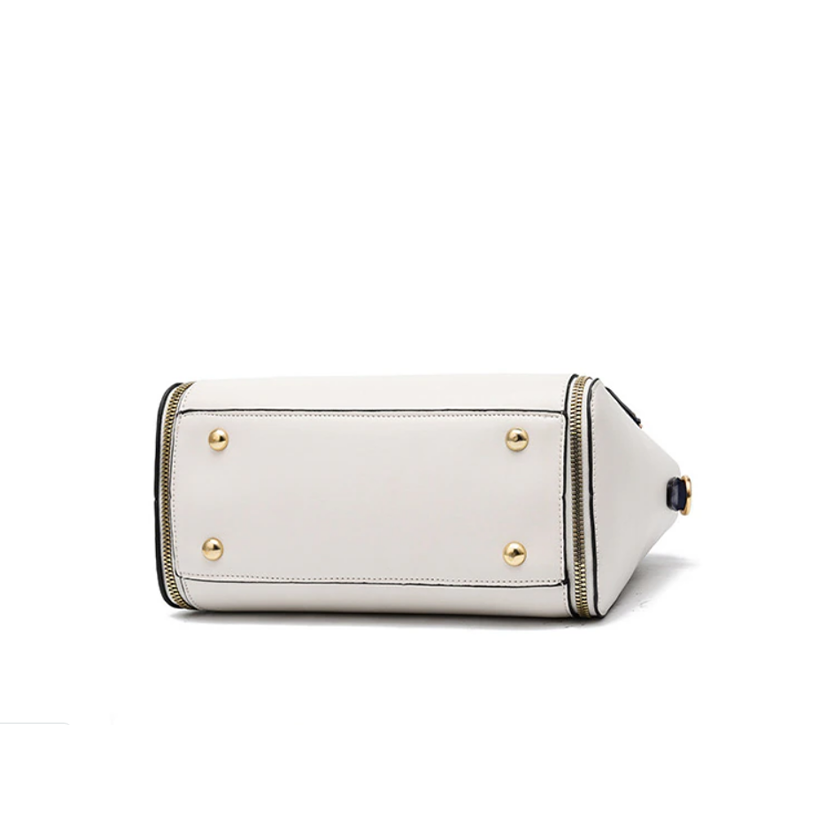 A white rectangular handbag shown from the bottom, featuring gold metal feet and black trim details.