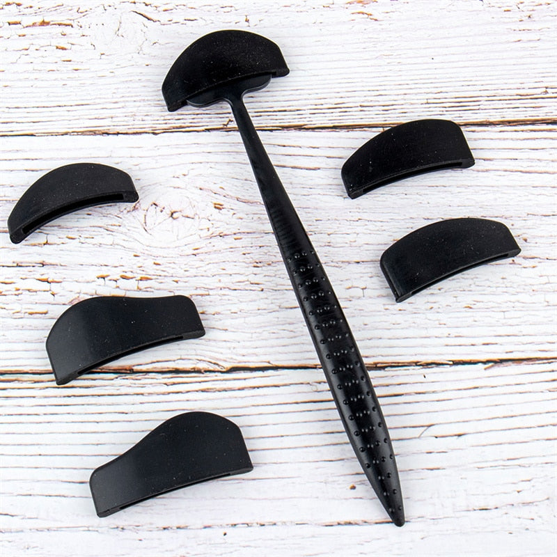Black denture brush with textured handle, surrounded by six black detachable covers, on a light wooden surface. Clean, organized, and simple.