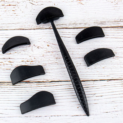 Black denture brush with textured handle, surrounded by six black detachable covers, on a light wooden surface. Clean, organized, and simple.