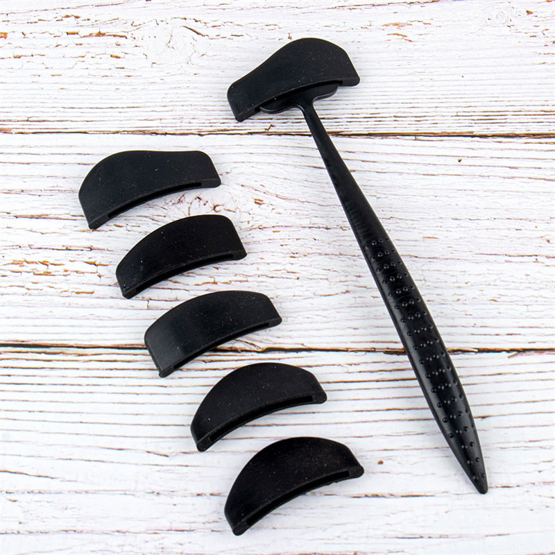 Black tool with curved attachments arranged on weathered white wood. The attachments are small and crescent-shaped, suggesting versatility and functionality.