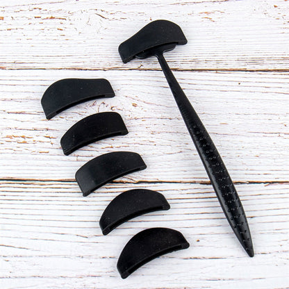 Black tool with curved attachments arranged on weathered white wood. The attachments are small and crescent-shaped, suggesting versatility and functionality.