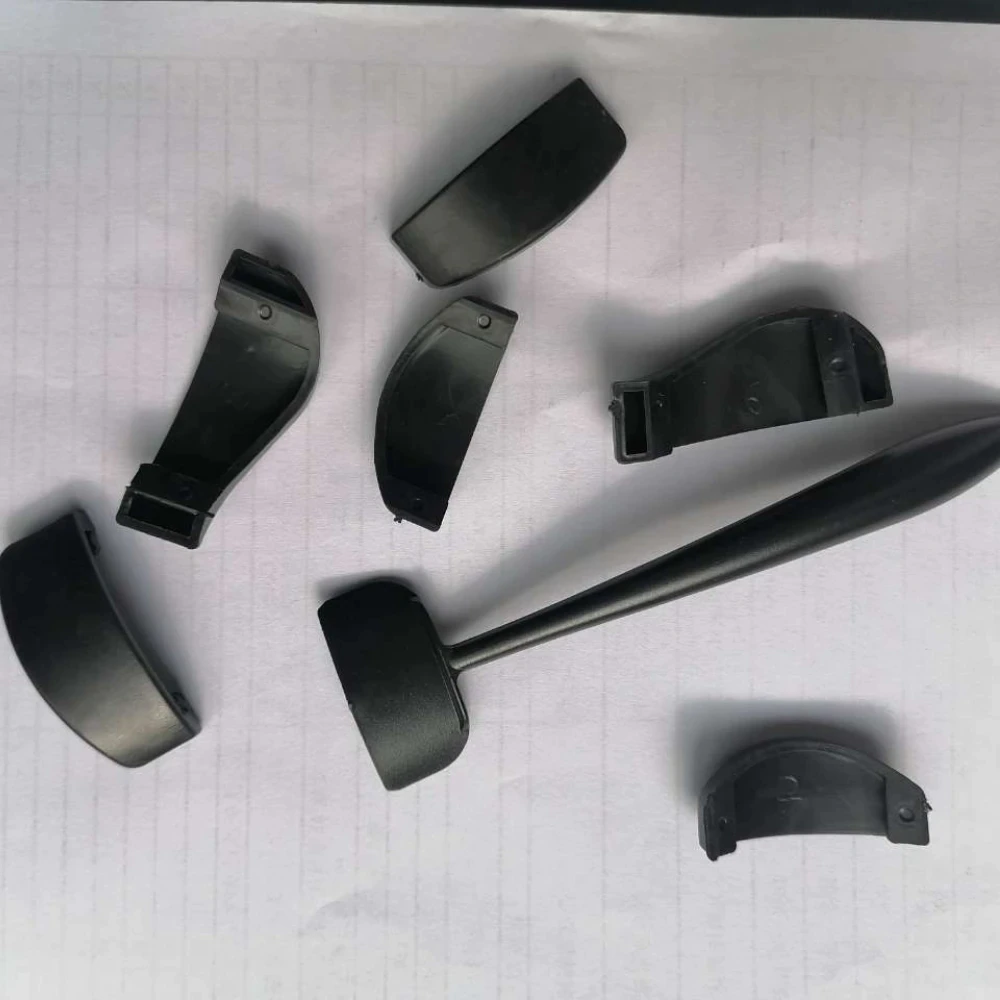 Broken black plastic coat hook pieces scattered on lined paper, showing a detached long handle and several curved segments, suggesting disassembly.