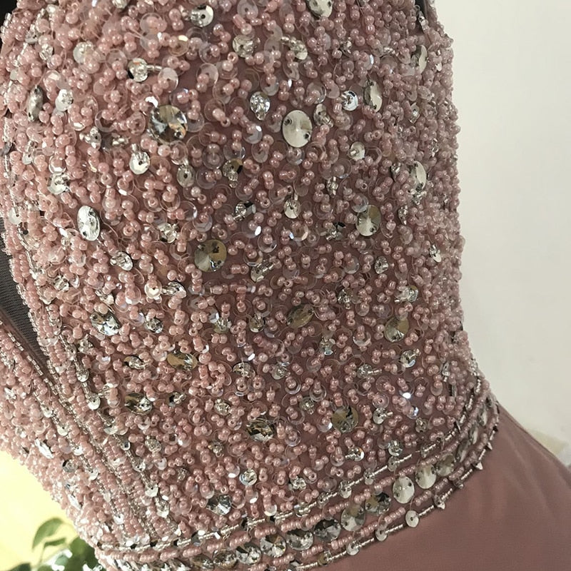 Close-up of a pink dress adorned with intricate beadwork and sequins, showcasing elegance and luxury. The details sparkle in soft light.