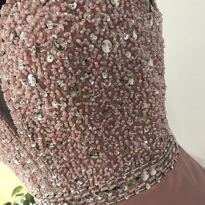 Close-up of a pink dress adorned with intricate beadwork and sequins, showcasing elegance and luxury. The details sparkle in soft light.