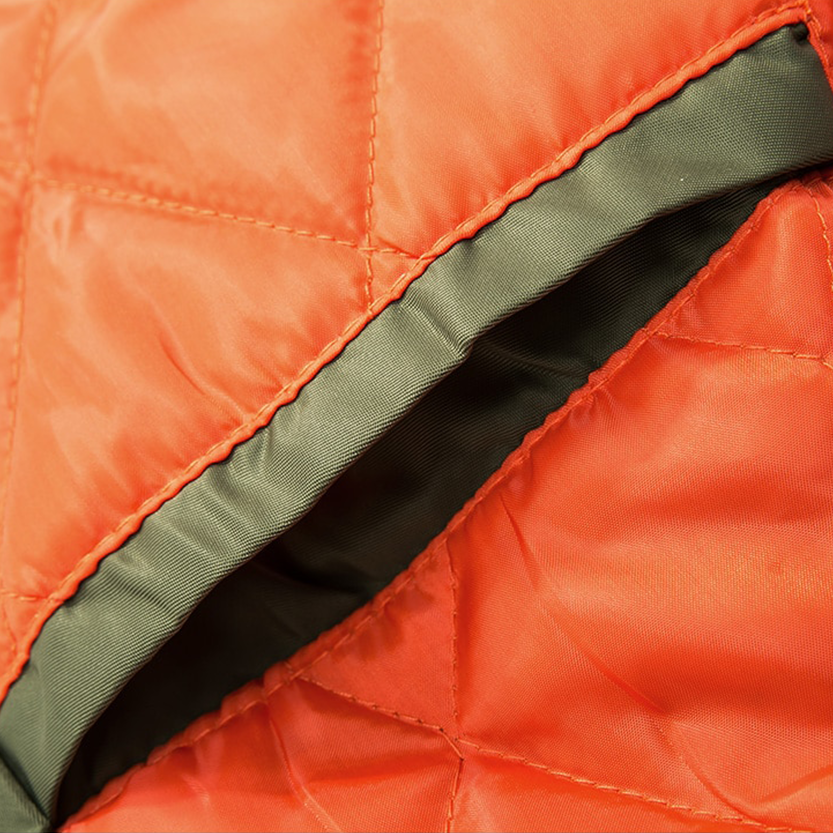 Close-up of an orange quilted jacket with visible stitching. A green interior lining peeks out from an open seam, conveying warmth and softness.