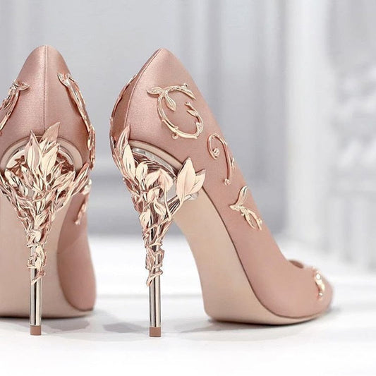 A pair of pink high heel stilettos with metallic floral designs on the heel.