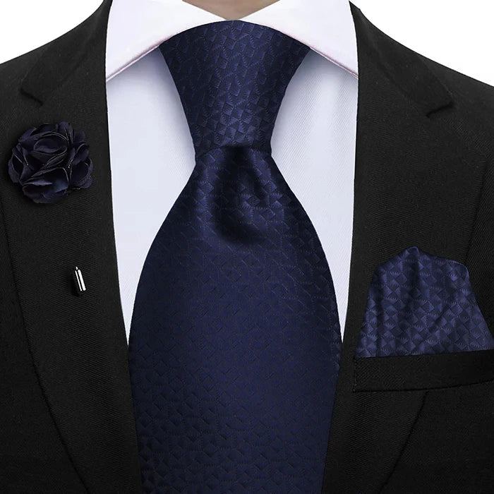 Navy blue tie with matching pocket square and lapel flower on a black suit.