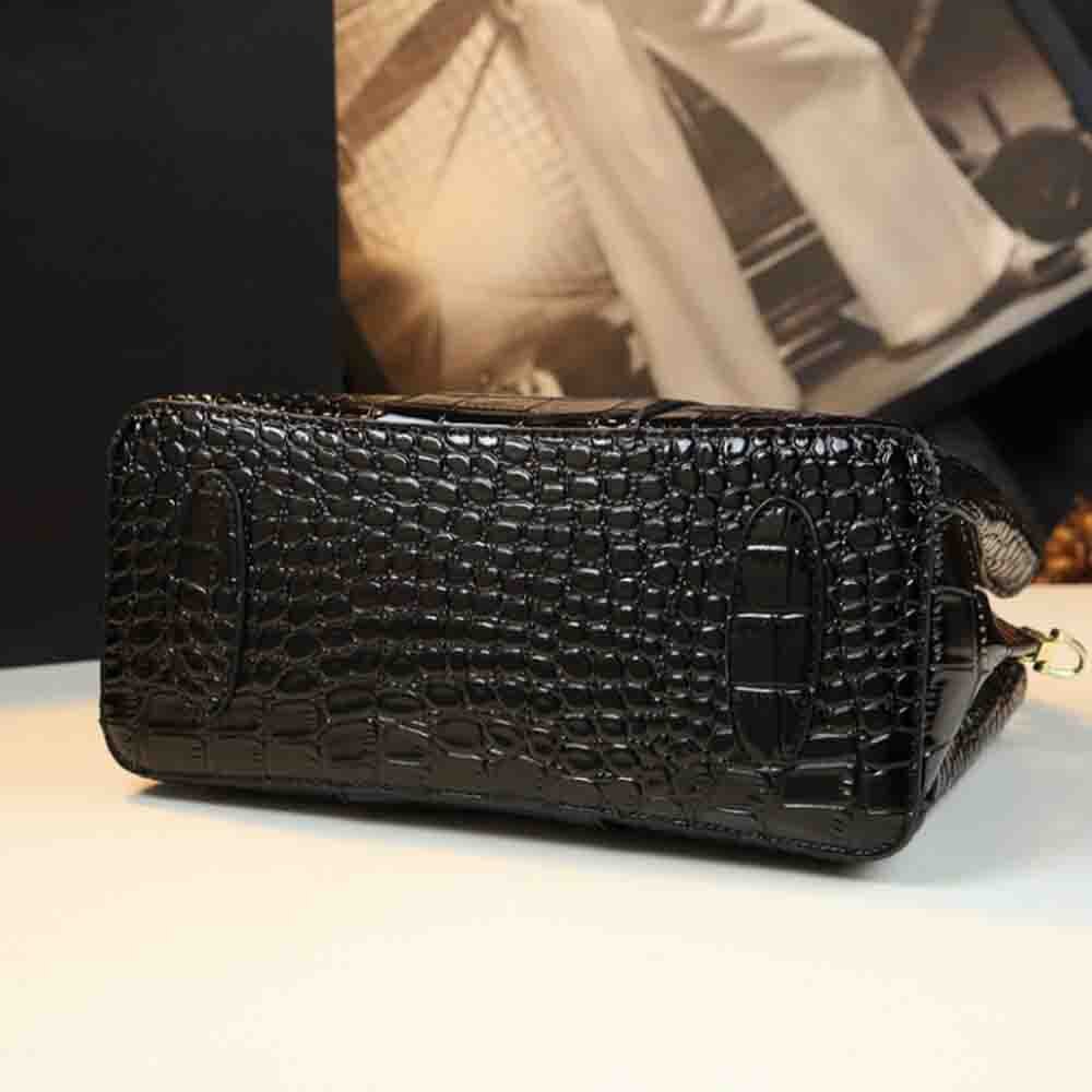 Sleek black crocodile-patterned handbag resting on a table with a blurred background of fashion imagery.