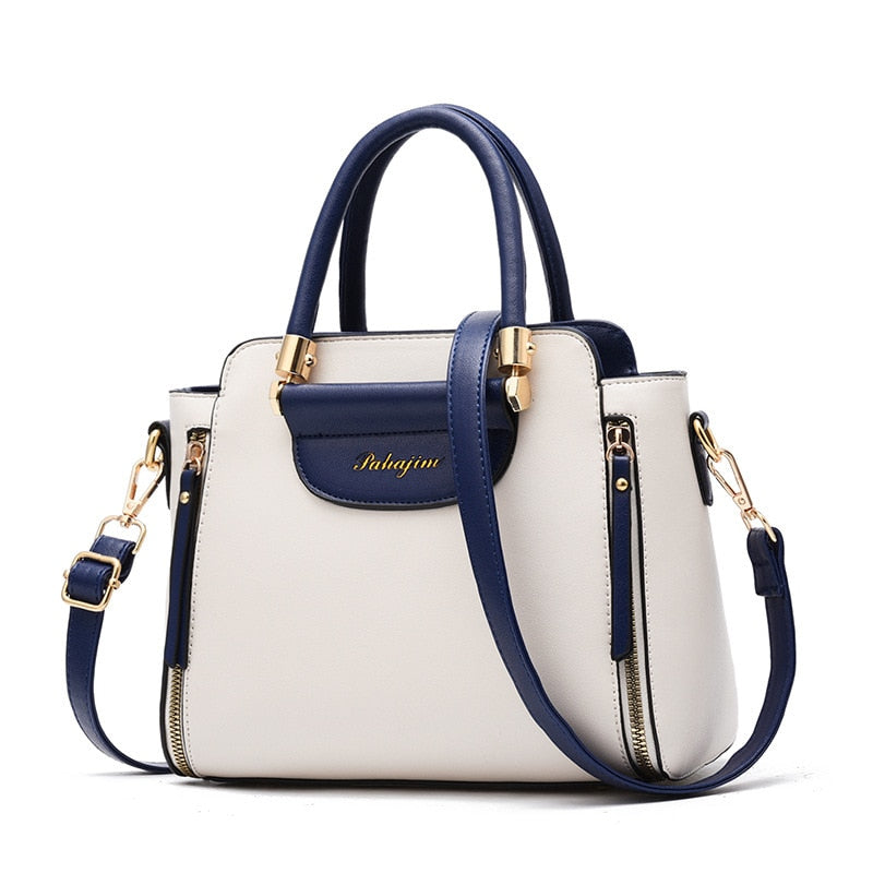 Stylish two-tone handbag in cream and navy blue, featuring gold accents and a removable strap for versatile carrying options.