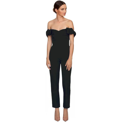Woman in a black, off-the-shoulder jumpsuit with ruffled sleeves and fitted pant legs. She stands confidently, looking to the side against a white background.