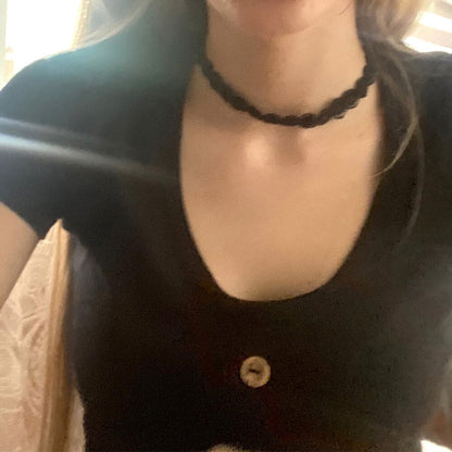 A woman wearing a black scoop-neck top and a black choker necklace. The image captures the neckline and shoulders, with soft natural lighting.