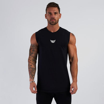A muscular man stands confidently in a black sleeveless shirt with a small white logo, set against a plain gray background.