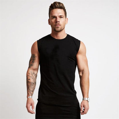 A muscular man in a fitted black sleeveless shirt stands confidently, showcasing his tattoos and a silver wristwatch.