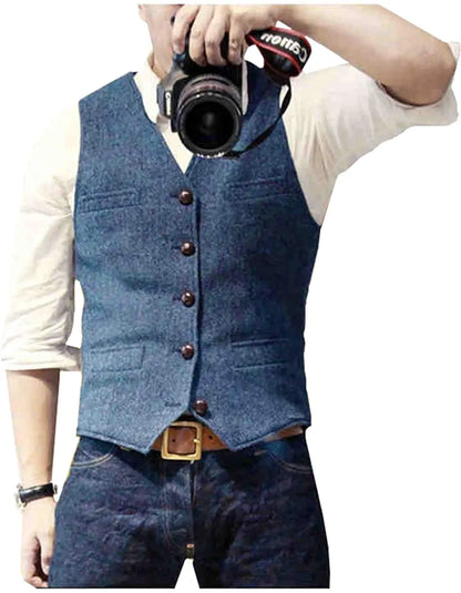 Man in a blue denim vest and beige shirt holding a camera, posing for a photo. Casual, stylish look with classic denim outfit.