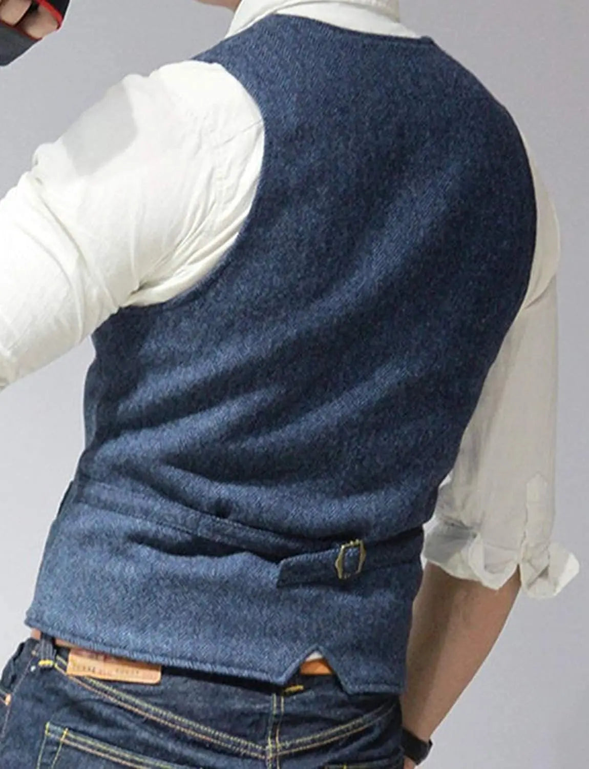 A man in a blue denim vest stands with his back facing the camera, wearing a white shirt and dark jeans.