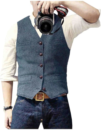 A man wearing a blue vest over a white shirt, holding a camera, stands against a white background.