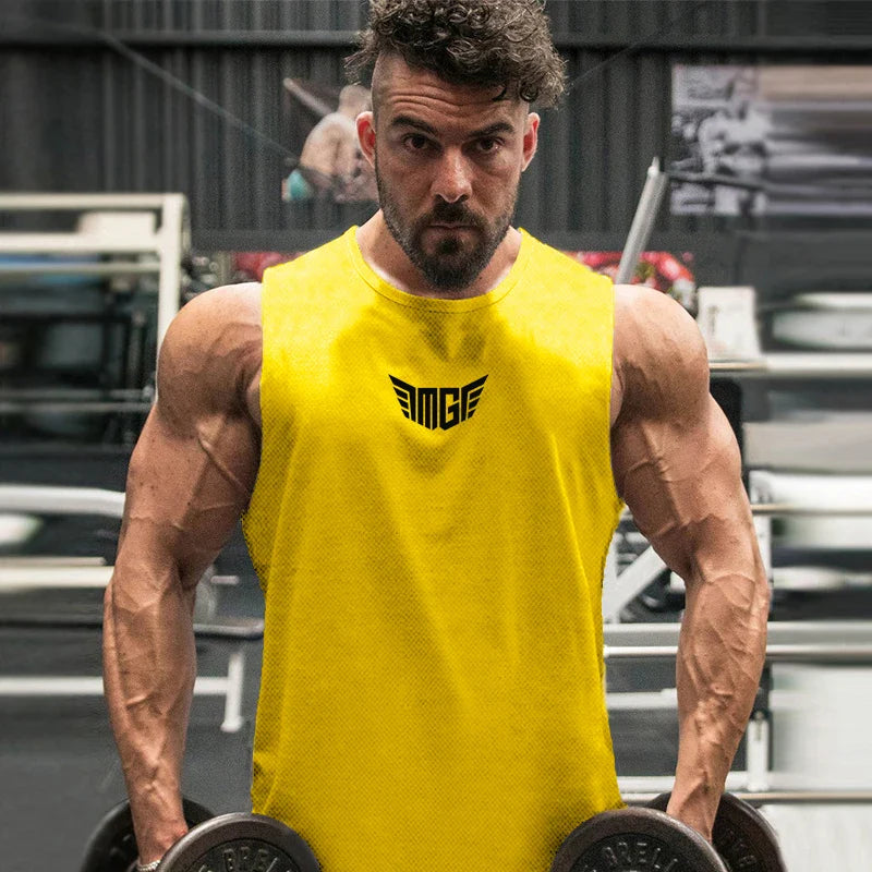 A muscular individual in a bright yellow sleeveless shirt holds two dumbbells in a gym setting. Equipment is visible in the background.