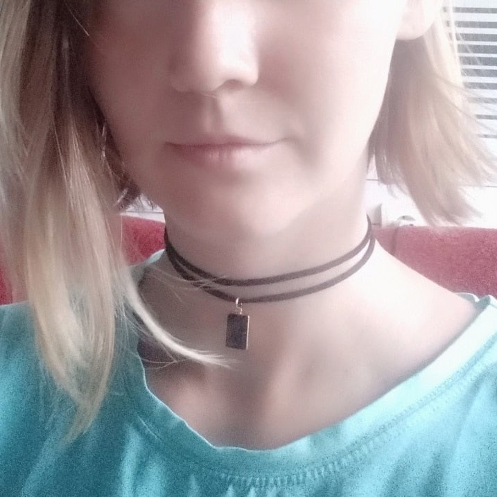 A woman with shoulder-length hair wears a turquoise shirt and a double-strand black choker with a small rectangular pendant, conveying a casual style.