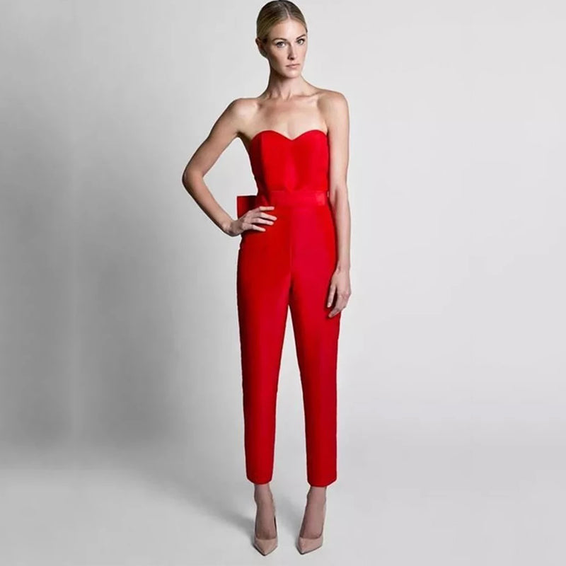 A woman in a fitted, strapless red jumpsuit poses confidently against a gray background