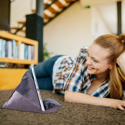 A person lounges on a carpeted floor with a tablet resting on a gray triangular pillow, surrounded by a cozy home environment.