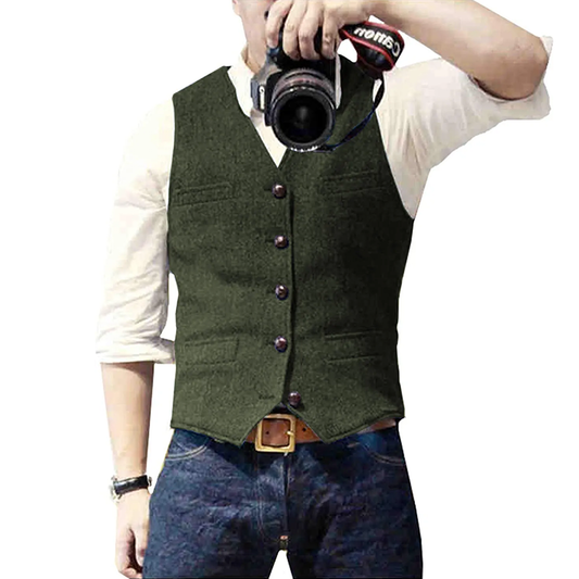 A man wearing a green vest and a white shirt poses while holding a camera, ready to take a photograph.