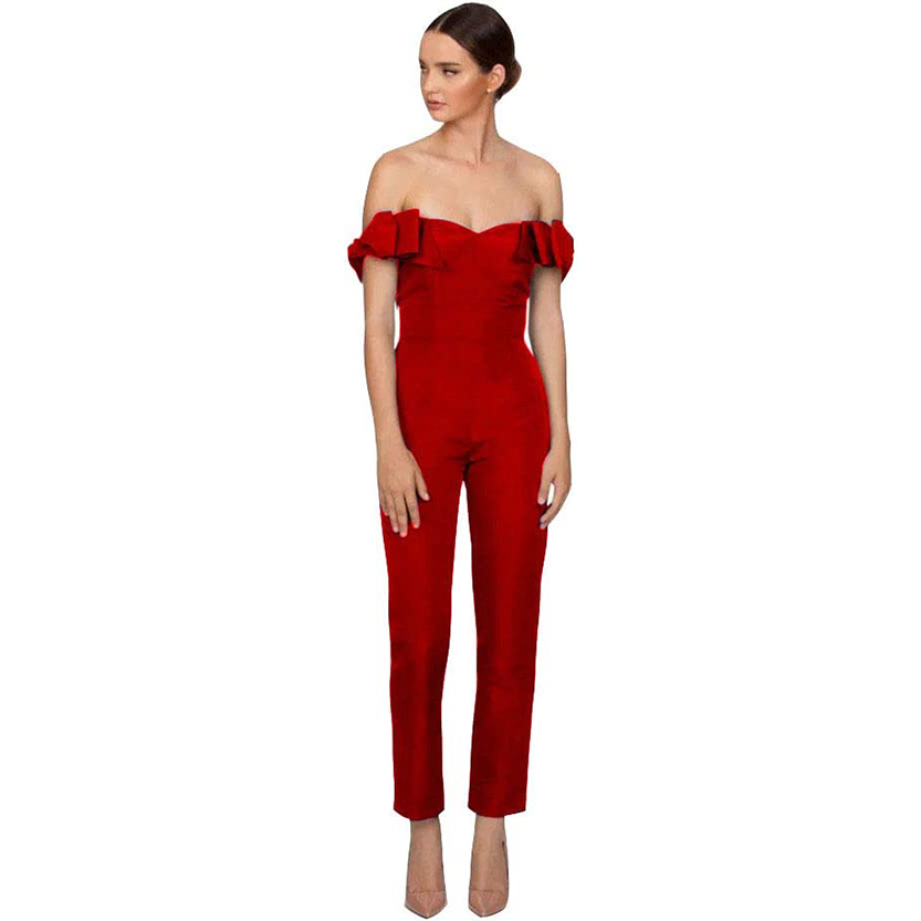 A woman in a red off-the-shoulder jumpsuit with ruffled sleeves stands against a white background. She exudes elegance, looking to the side.