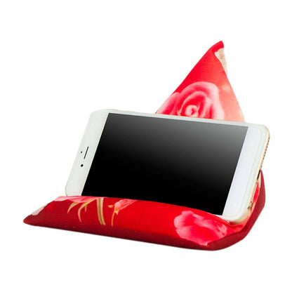 A smartphone resting on a red, triangular phone holder with a rose pattern, designed for hands-free viewing.