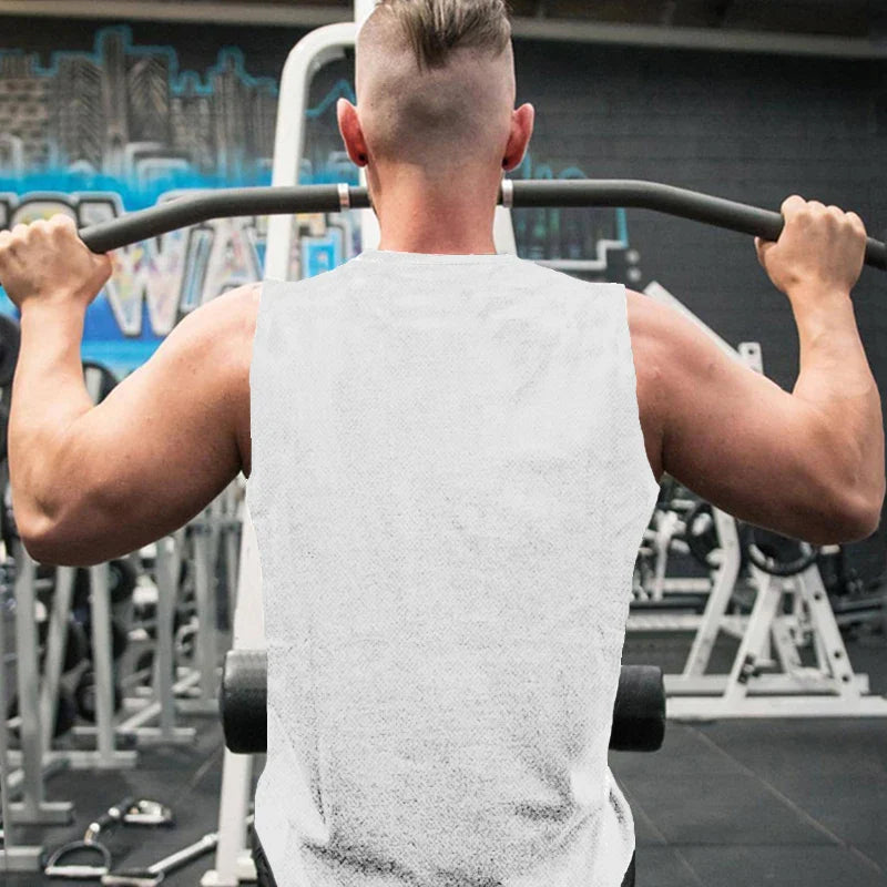 A muscular man in a sleeveless shirt performs a pull-up in a gym, with exercise equipment and graffiti visible in the background.