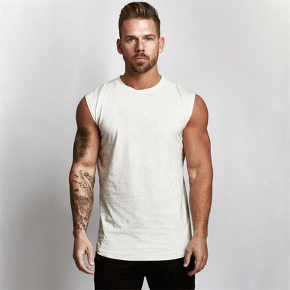 A muscular man wearing a sleeveless white t-shirt stands confidently, showcasing his arm tattoos against a neutral background.