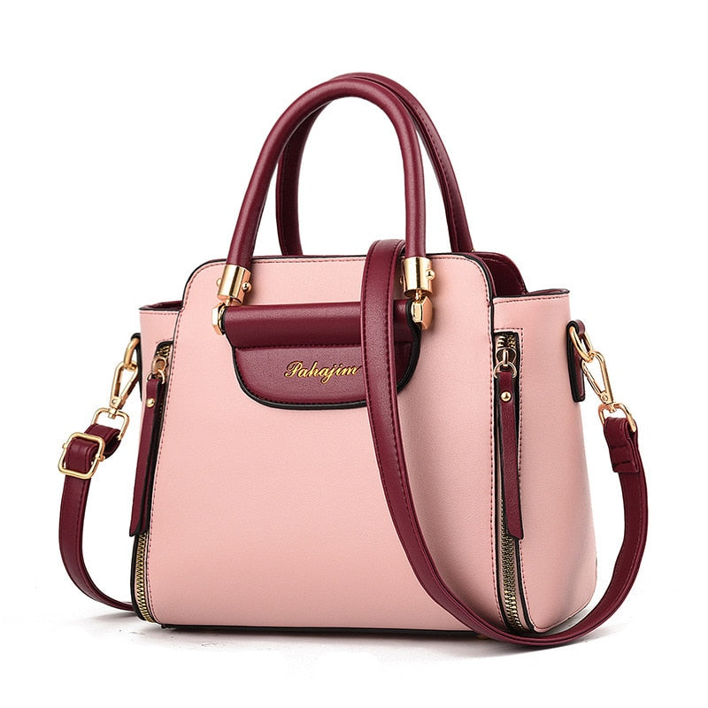 Stylish two-tone handbag with a soft pink body and burgundy accents, featuring gold hardware and a removable strap for versatility.