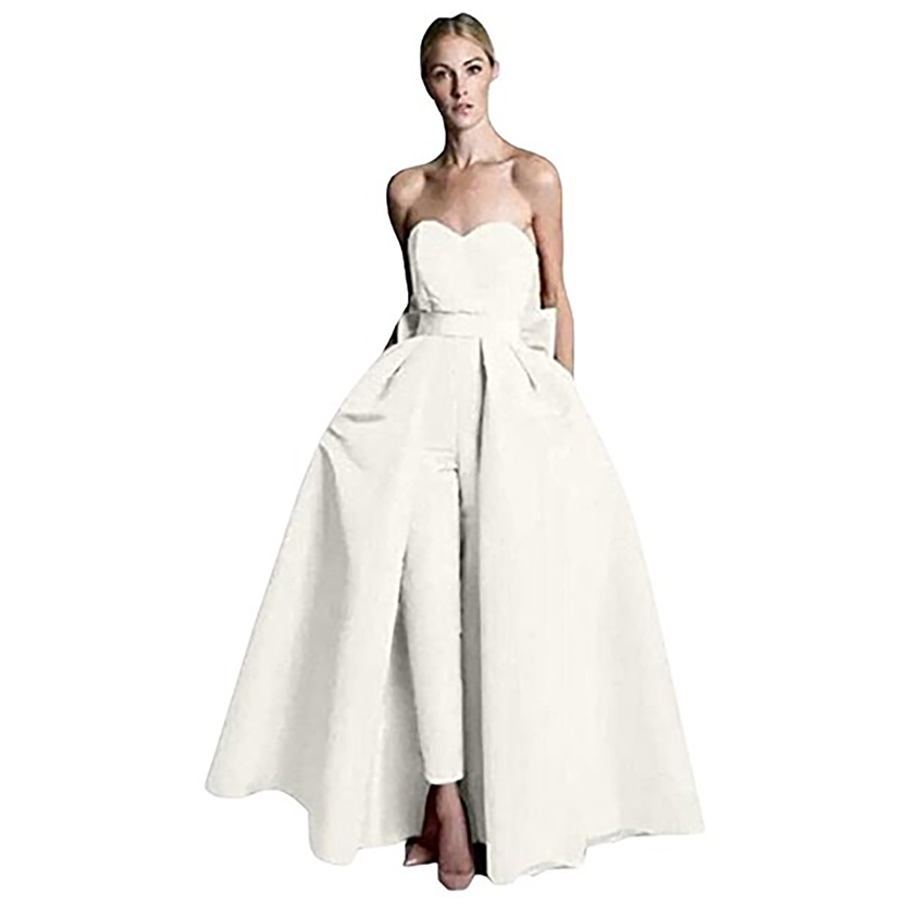 A woman wearing a strapless white gown featuring a fitted bodice, flowy overskirt, and sleek pants. The look is elegant and modern.