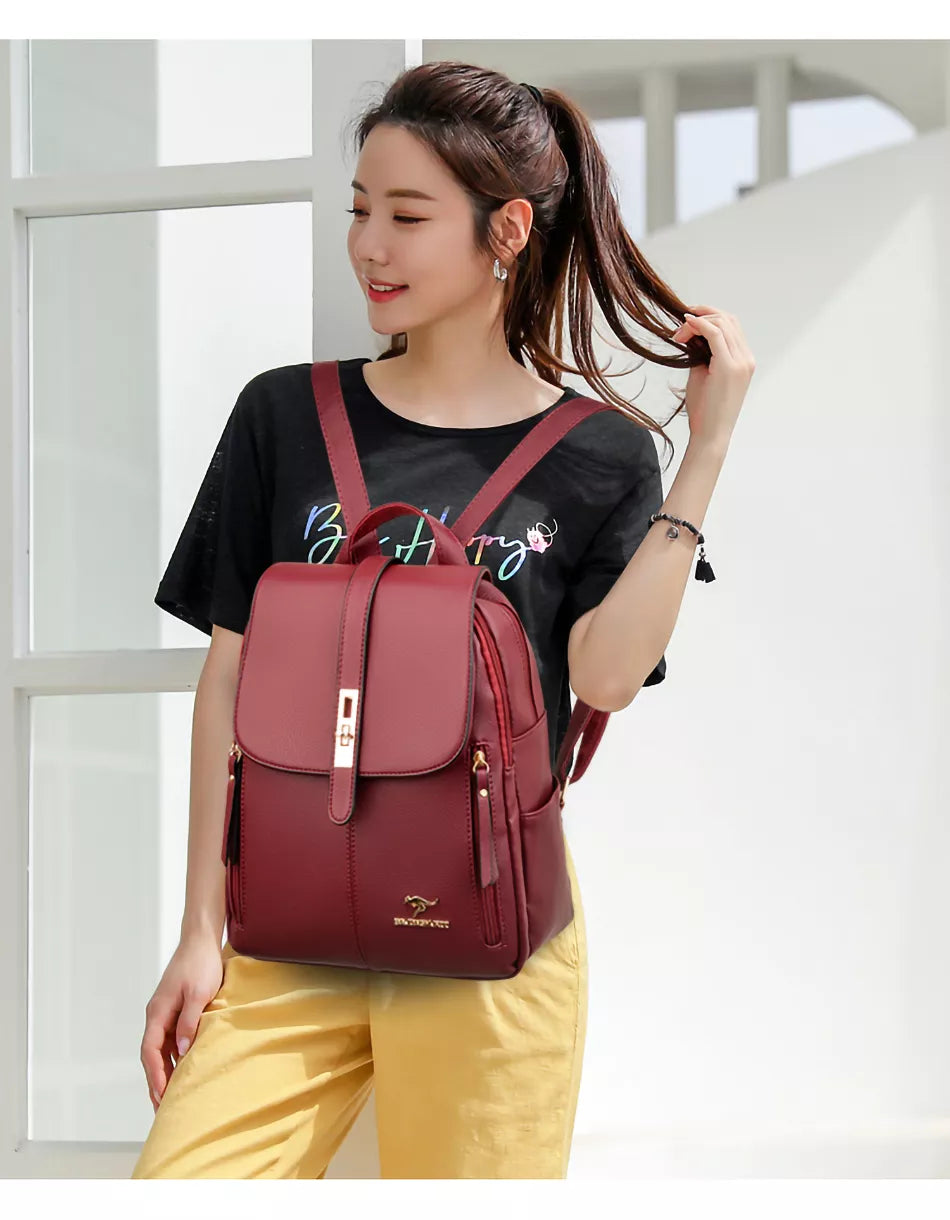 A person stands in a bright space wearing a black t-shirt and yellow pants, holding a stylish maroon backpack with gold accents.