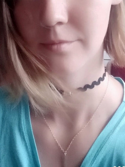 Close-up of a woman wearing a wave-patterned choker and a delicate chain necklace. Her expression is serene and she wears a turquoise top.