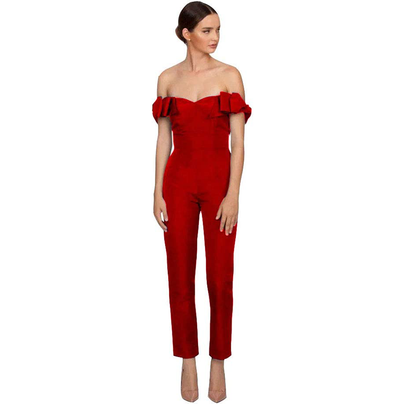Woman in an elegant red, off-shoulder jumpsuit with ruffle details, poses confidently. She wears nude heels, exuding a sophisticated and chic vibe.