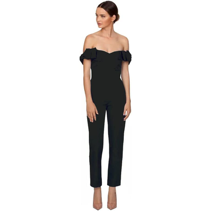 A woman wearing an off-shoulder black jumpsuit with ruffle sleeves and nude heels stands against a white background, looking confidently to the side.