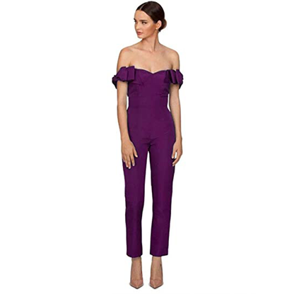 Woman in an off-shoulder purple jumpsuit with ruffled sleeves stands confidently. 