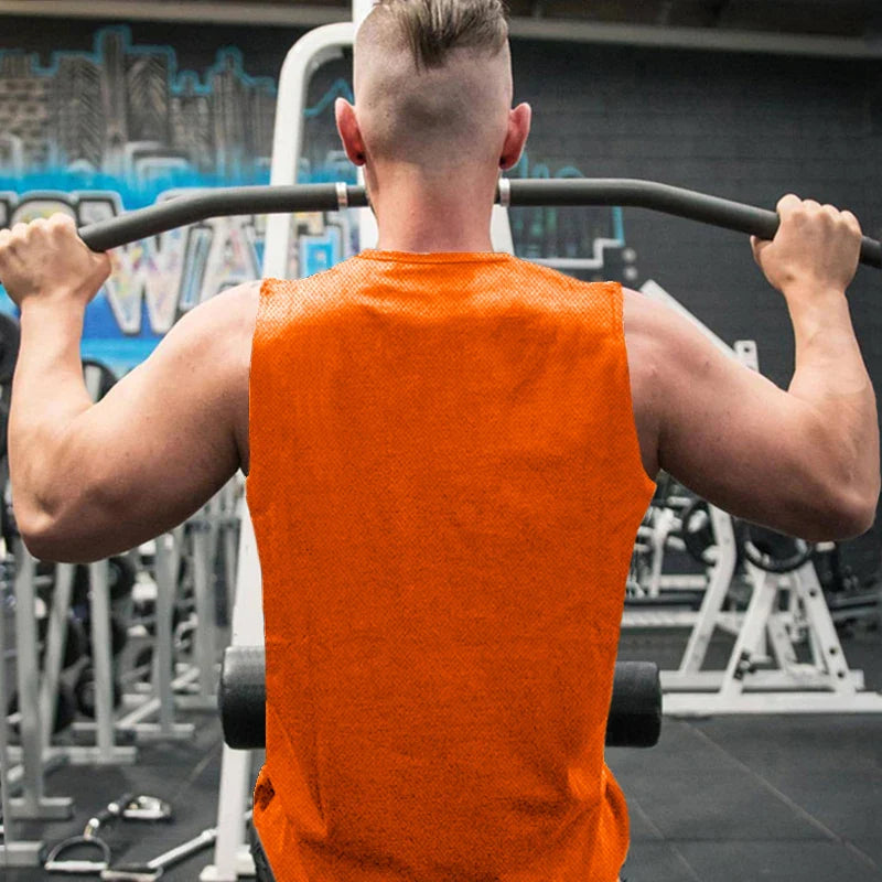A muscular man in an orange sleeveless shirt performs a pull-up at the gym, showcasing his strong arms against a vibrant mural.