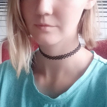 A woman wears a black choker and a pale blue shirt, looking serene. The close-up focuses on their neck and lower face.
