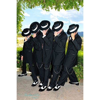 Five people dressed in black suits and white hats lean synchronously on a sunny day, set against a lush green backdrop under a leafy arch.