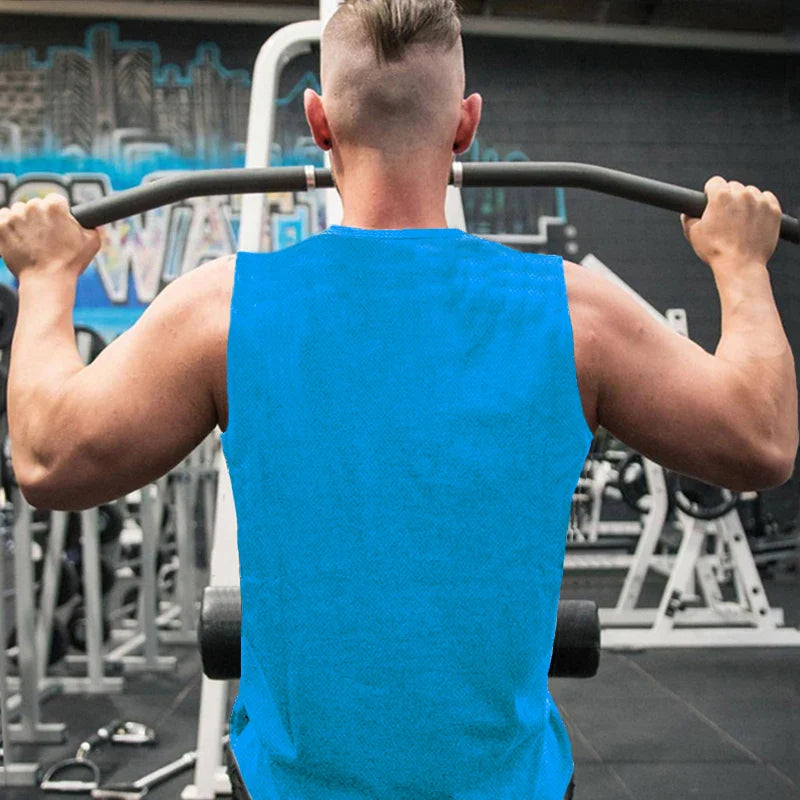 A muscular person in a blue tank top performs a pull-up in a gym, with exercise equipment and a colorful mural in the background.