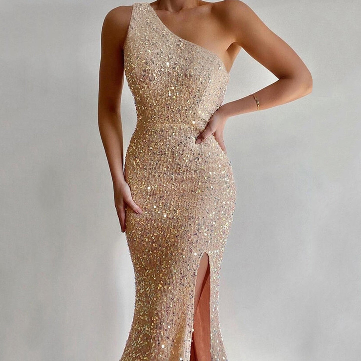 A woman wearing a shimmering, one-shoulder, champagne-colored evening gown adorned with sequins. The dress features a thigh-high slit, exuding elegance.
