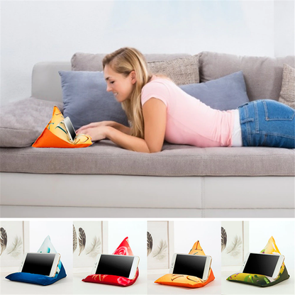 A woman lies on a couch, using a colorful phone holder shaped like a triangular pillow to watch her device comfortably.