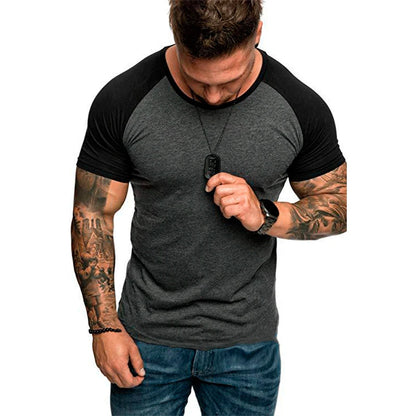 Man wearing a black and gray t-shirt with tattoos on arms, holding sunglasses.