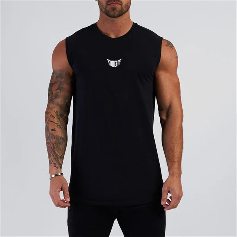 A muscular man wearing a sleeveless black shirt with a white logo, showcasing his tattoos against a plain light background.
