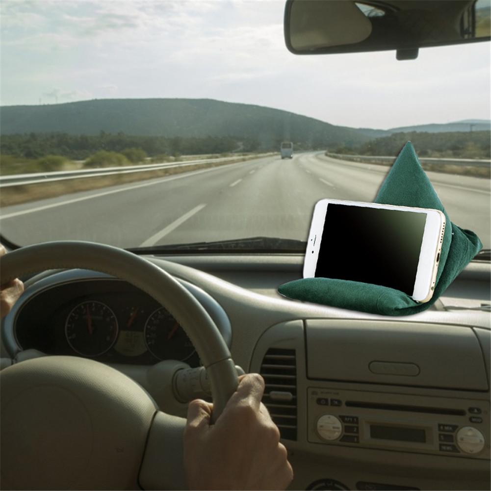 A driver holds the steering wheel, while a phone sits on a green fabric stand on the dashboard, with a scenic road ahead.